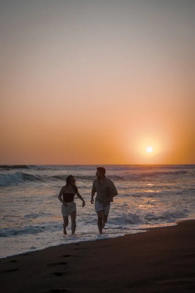 Shanice und ihr Freund Fabian laufen lachend bei Sonnenuntergang durchs Wasser am Strand auf Bali