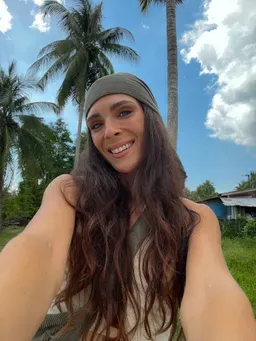 Shanice lächelt mit Haarband vor Palmen und blauem Himmel